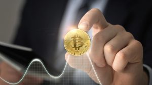 Uma mão segurando uma moeda dourada de Bitcoin, simbolizando o investimento em criptomoedas e a revolução digital no setor financeiro. No fundo, um gráfico ilustrando a volatilidade do mercado de criptoativos destaca as oscilações do valor do Bitcoin. A imagem transmite inovação, tecnologia e oportunidades no mundo dos investimentos digitais.