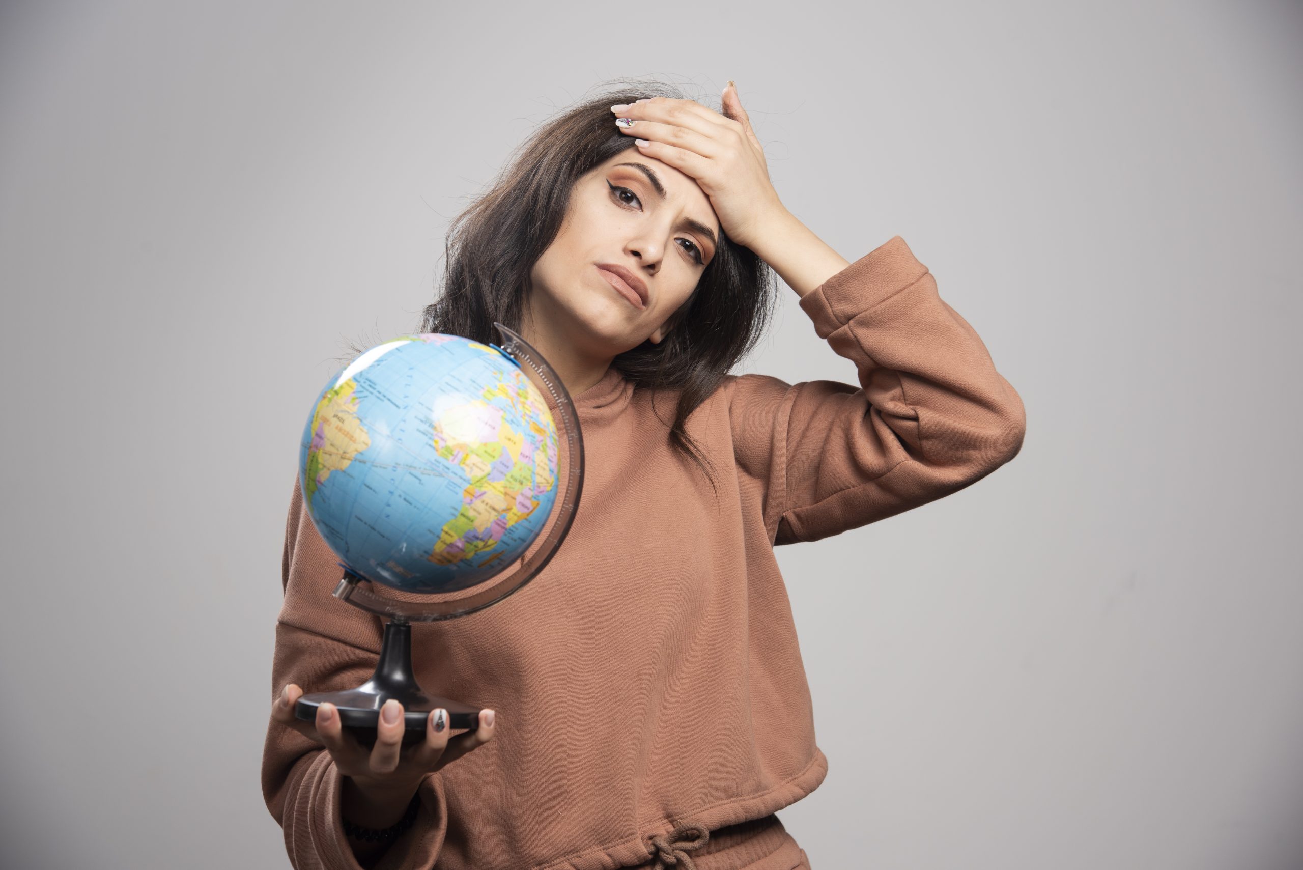 Mulher com expressão preocupada segurando um globo terrestre em uma mão enquanto apoia a outra sobre a testa, demonstrando cansaço ou inquietação. A imagem simboliza a preocupação crescente com o impacto das mudanças climáticas nas finanças pessoais, refletindo os desafios que eventos climáticos extremos, inflação verde e crises ambientais impõem ao orçamento familiar e ao planejamento econômico global.
