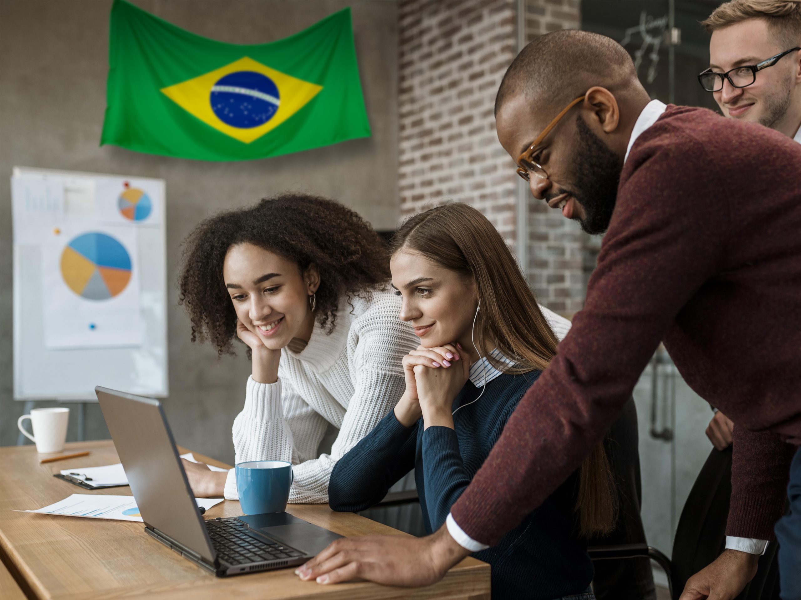 Grupo de quatro jovens profissionais reunidos em frente a um notebook, analisando dados com atenção e entusiasmo em um ambiente de escritório moderno. Ao fundo, há gráficos de desempenho e uma bandeira do Brasil pendurada na parede. A cena representa um ambiente de inovação e colaboração, destacando o papel das fintechs no acesso ao crédito e às soluções bancárias no Brasil, promovendo inclusão financeira e novas oportunidades para a população.