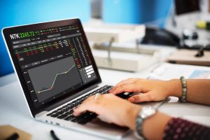 Pessoa analisa gráficos e cotações em tempo real em um notebook com interface de mercado financeiro, em um ambiente de trabalho, ilustrando a avaliação de investimentos em fundos cambiais para proteger o portfólio da variação do dólar.