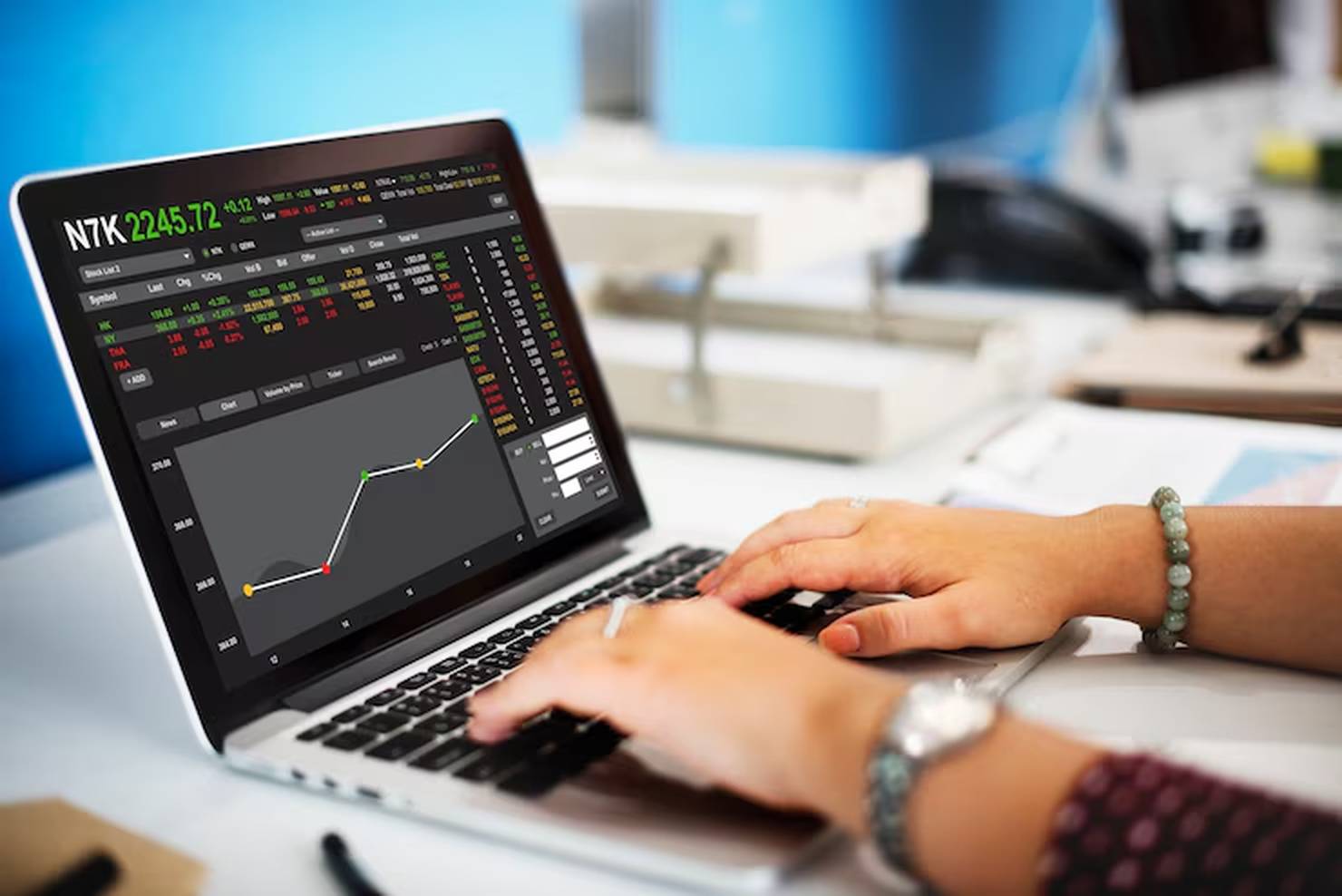 Pessoa analisa gráficos e cotações em tempo real em um notebook com interface de mercado financeiro, em um ambiente de trabalho, ilustrando a avaliação de investimentos em fundos cambiais para proteger o portfólio da variação do dólar.