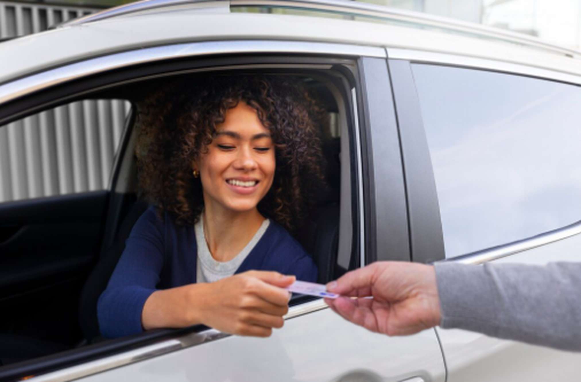 Mulher dentro do carro sorridente, entregando um cartão para pagamento, representando praticidade e as vantagens dos cartões de crédito com benefícios para motoristas de aplicativo.