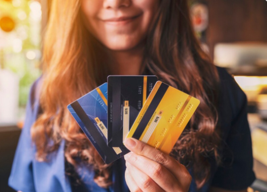 Mulher sorridente segurando três cartões de crédito coloridos em leque, representando opções de cartões co-branded que oferecem benefícios e vantagens em parcerias com lojas e empresas.