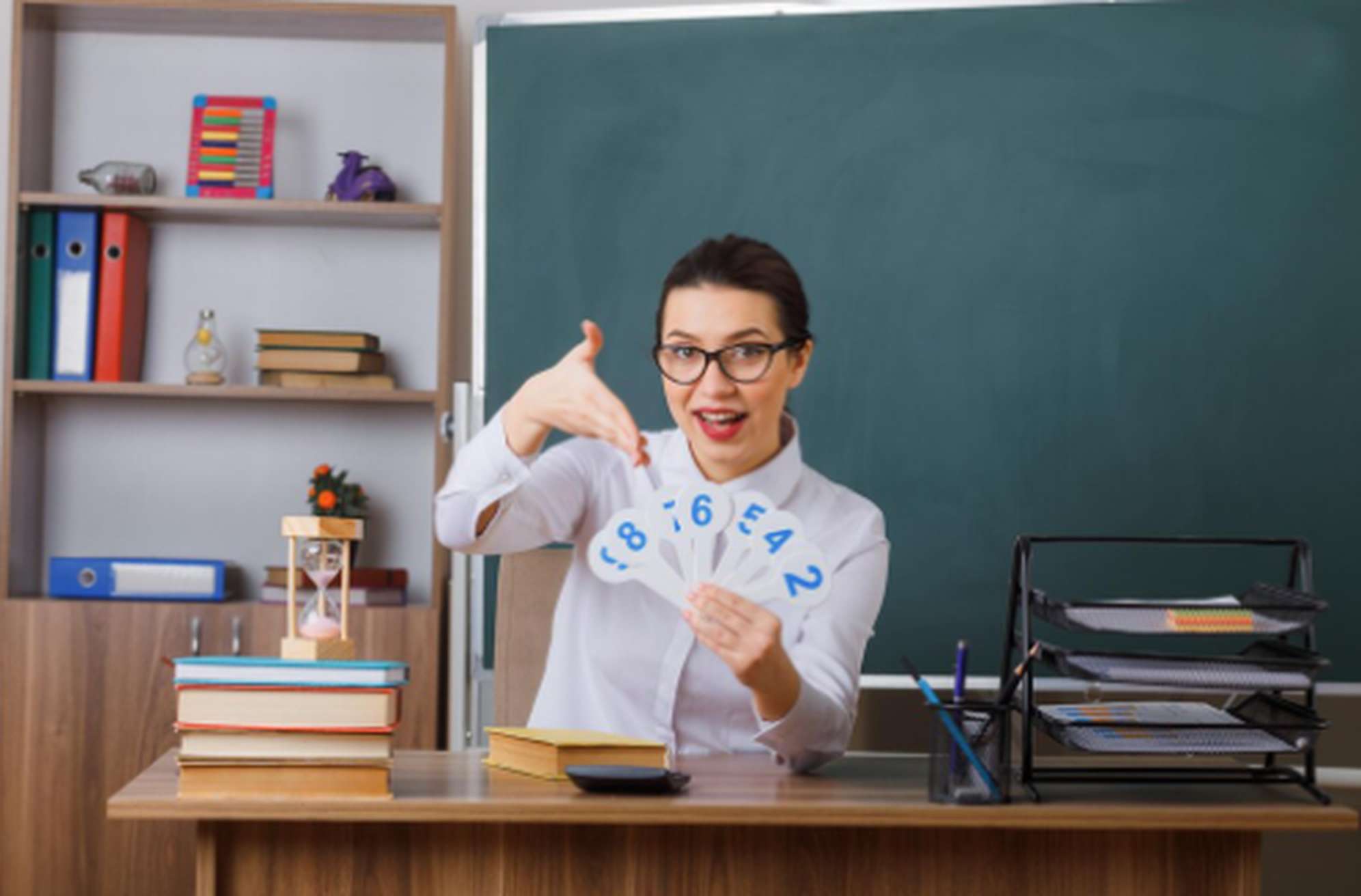 Professora sorridente em sala de aula, mostrando cartões com números para explicar conceitos, simbolizando a importância da educação financeira no aprendizado e no desenvolvimento das habilidades de gestão do dinheiro.