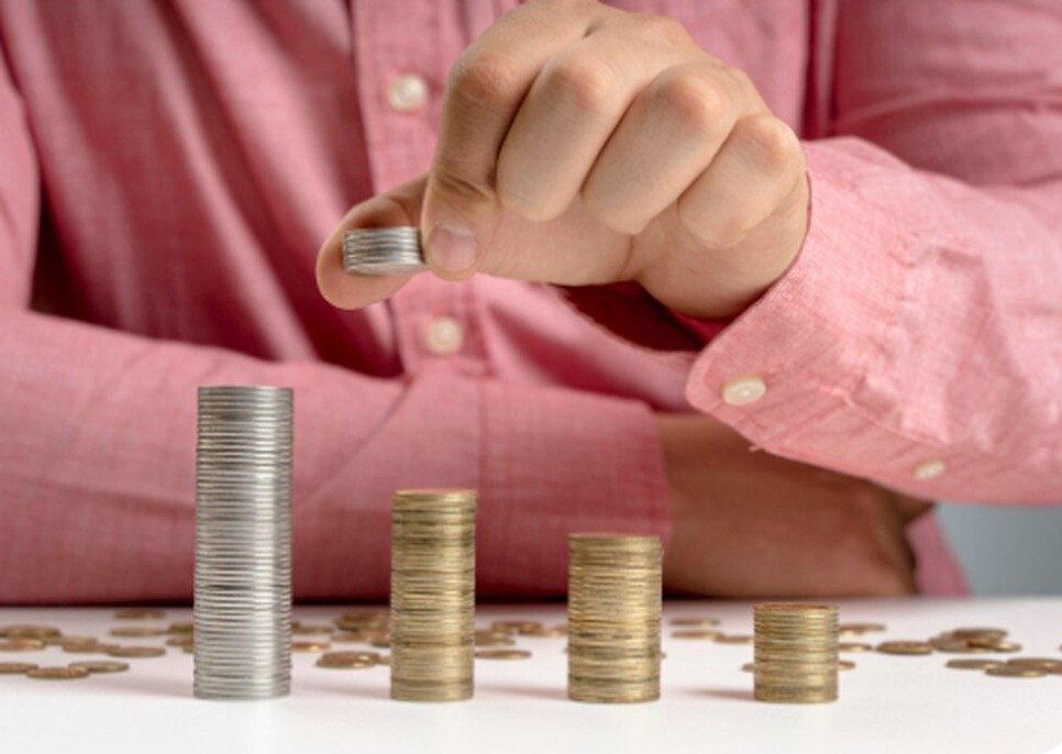 Mão empilhando moedas em diferentes alturas sobre uma mesa, simbolizando crescimento financeiro e estratégias de investimento em precatórios para obter rentabilidade a longo prazo.