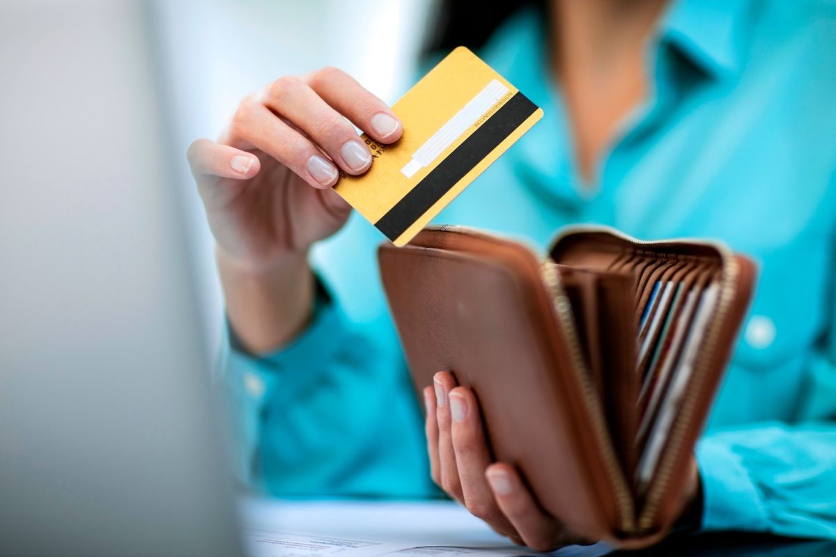 Pessoa segurando uma carteira de couro aberta e retirando um cartão bancário amarelo, representando praticidade no uso de cartões com funcionalidades multi-moeda para compras e transações internacionais.